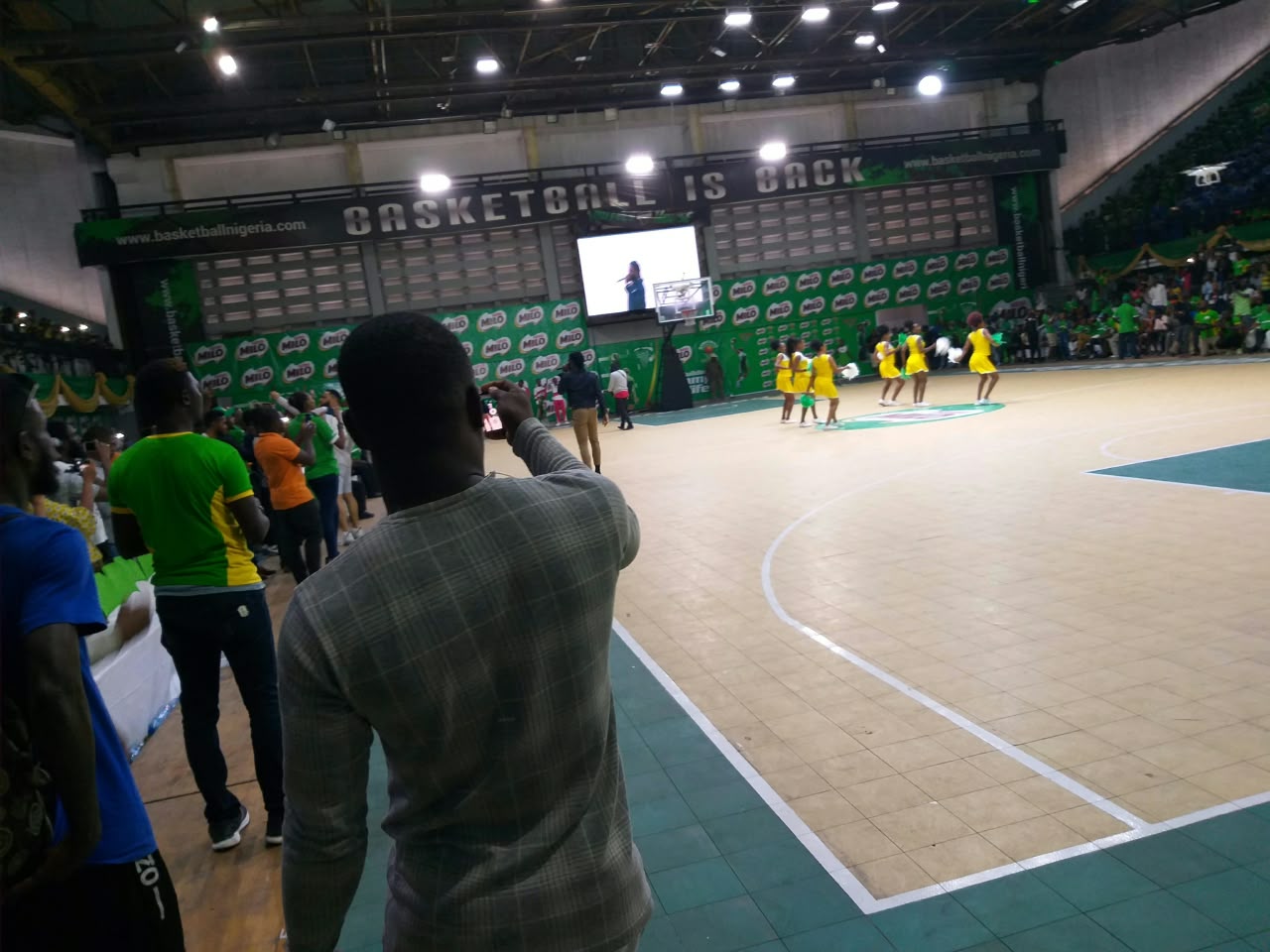 Milo basketball event: performers in yellow on the court with spectators courtside
